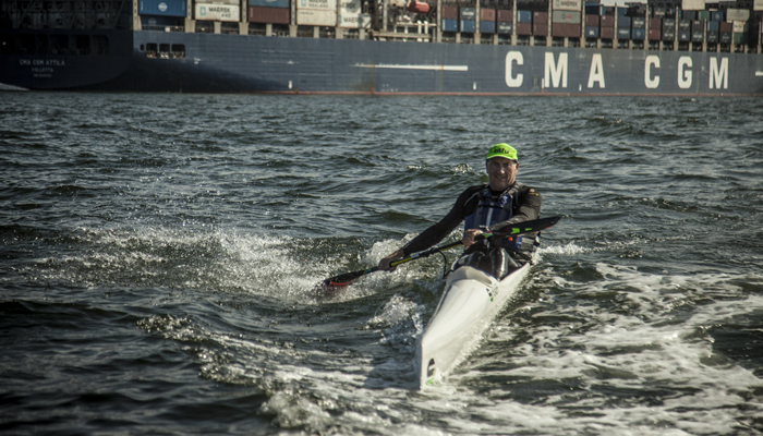Richard Kohler paddling past a container ship, dwarfed by its hull