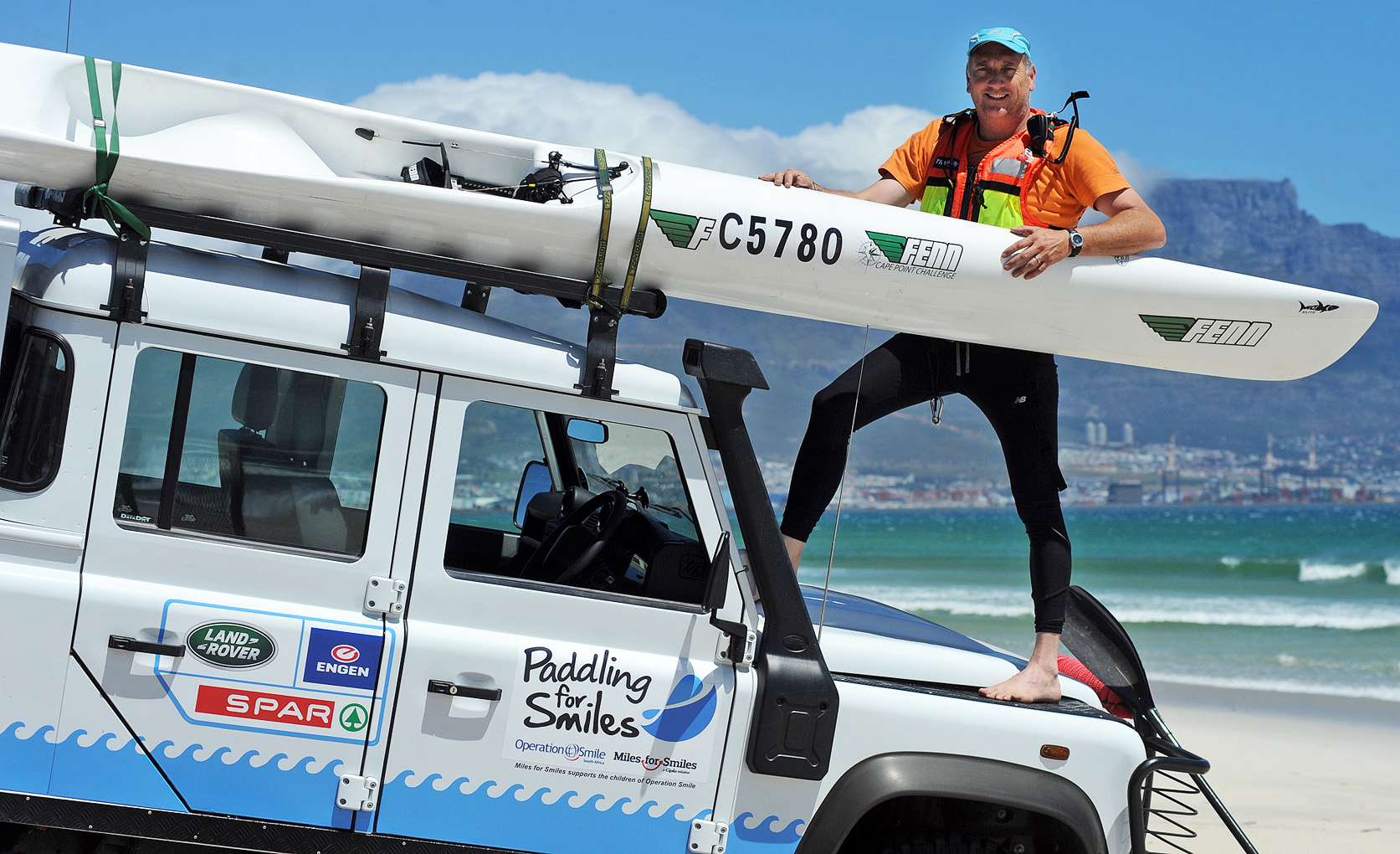 Richard Kohler celebrating on the beach with his surf ski held overhead, Table Mountain behind