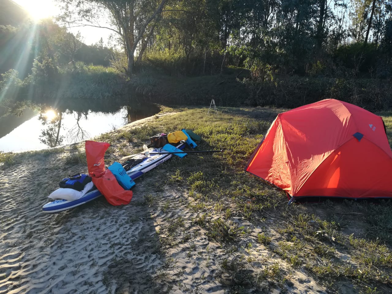 Tent and loaded SUP board camped on the riverbank
