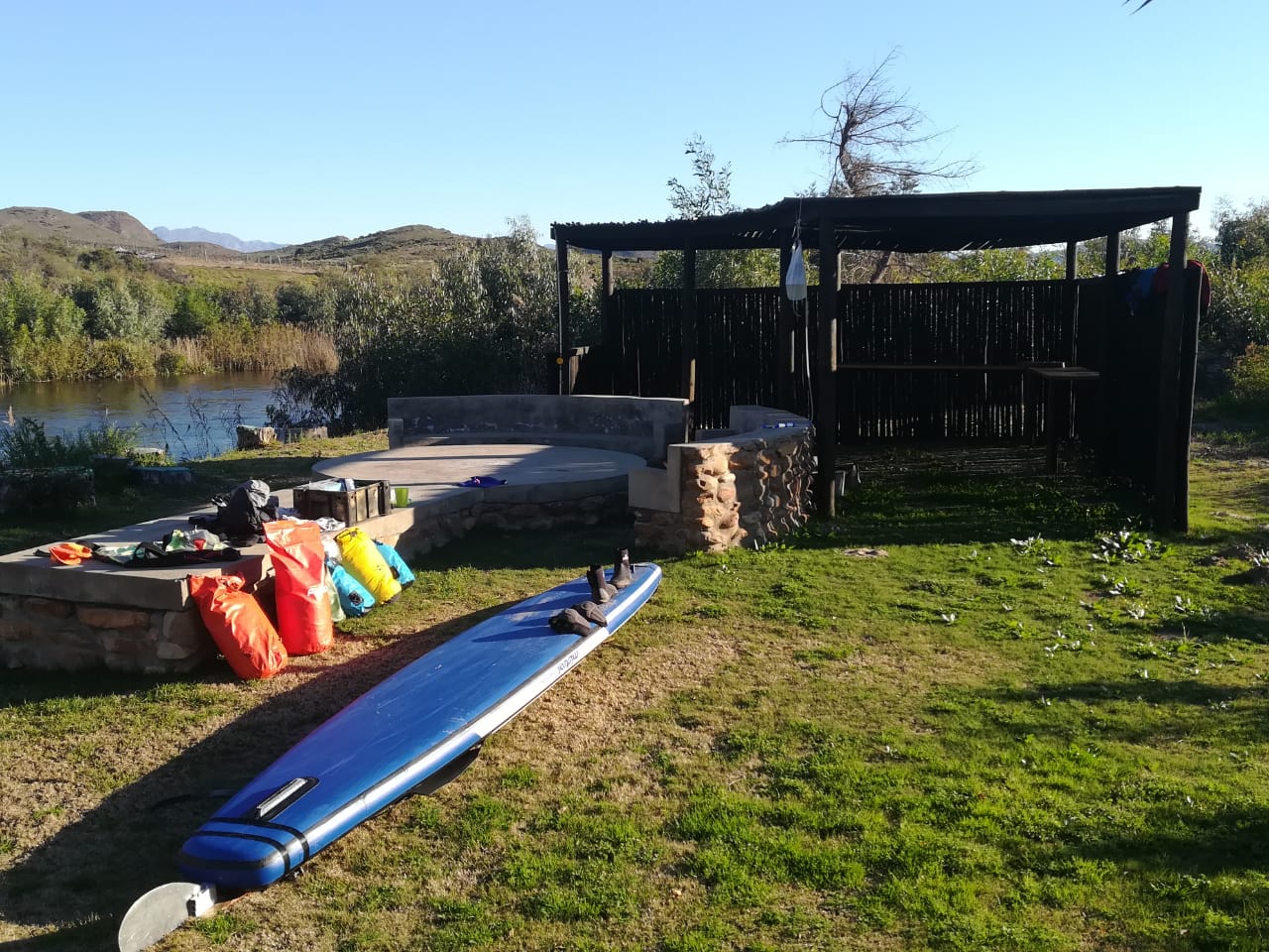 Dry bags, board and boots laid out at the riverside campsite